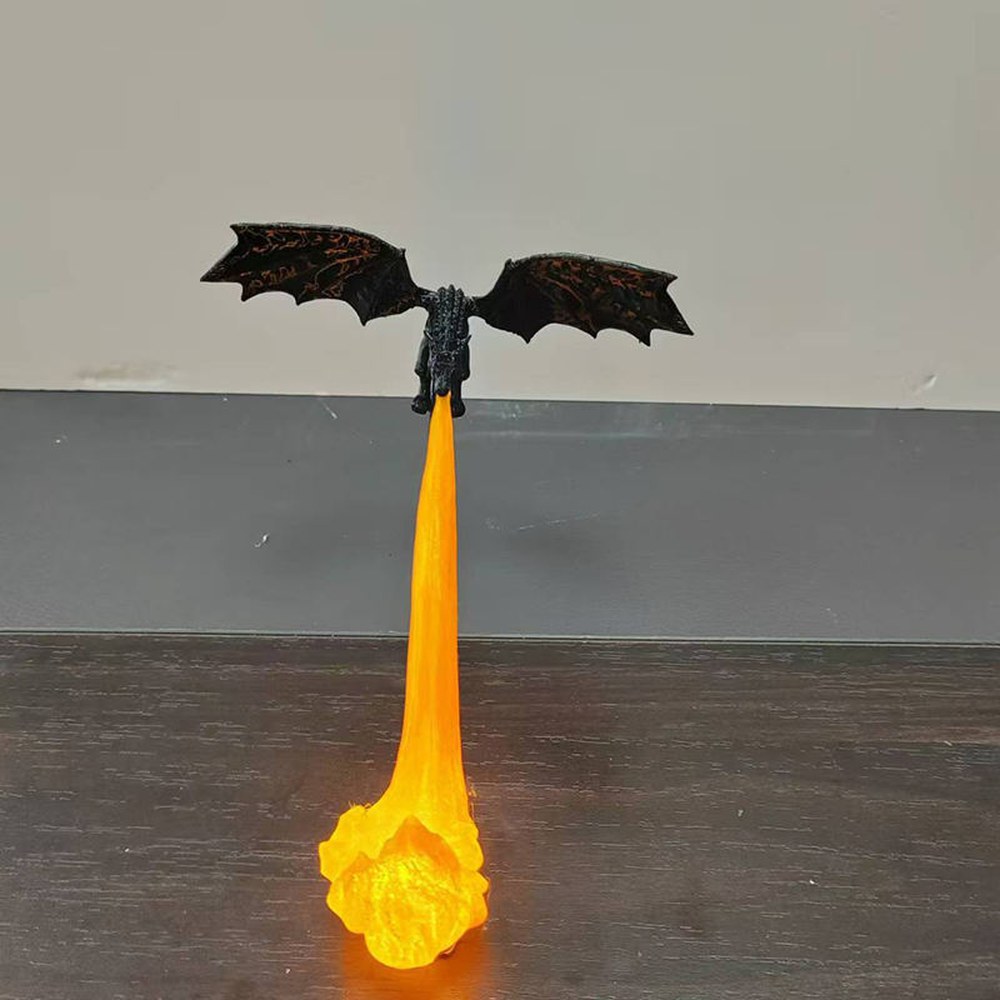 Dragon bookshelf light lit with an orange flame, standing on a wooden desk